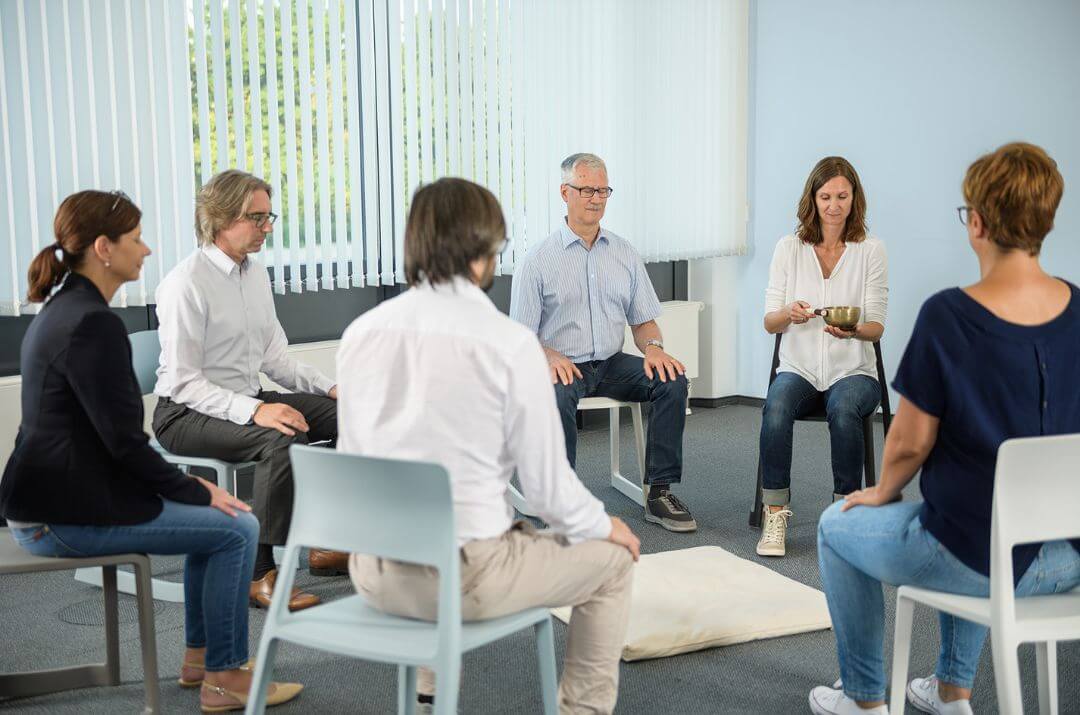 Eine Gruppe von Teilnehmer:innen sitzt im Achtsamkeitskurs „Abenteuer Achtsamkeit“, während Tina Klein eine Meditation anleitet.